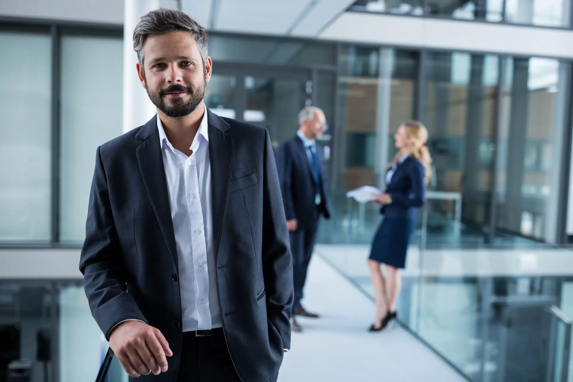 Businessman standing in office corridor and colleagues talking in background
