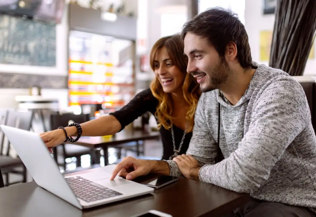 Happy young couple using laptop in a pub